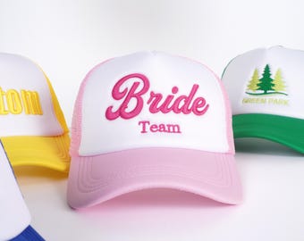 Könnte beinhalten: Rosa-weiße Trucker-Kappe mit dem Text "Bride Team" in rosa kursiver Schrift.