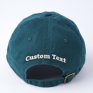 May include: A teal blue baseball cap with an adjustable strap and white embroidered text that says "Custom Text".