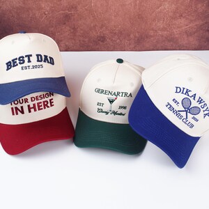 May include: Three baseball caps with embroidered designs. One cap is white with a blue brim and the text "BEST DAD EST.2025". Another is white with a green brim and a martini glass graphic. The third is white with a blue brim and "DIKAWSYK TENNIS CLUB".