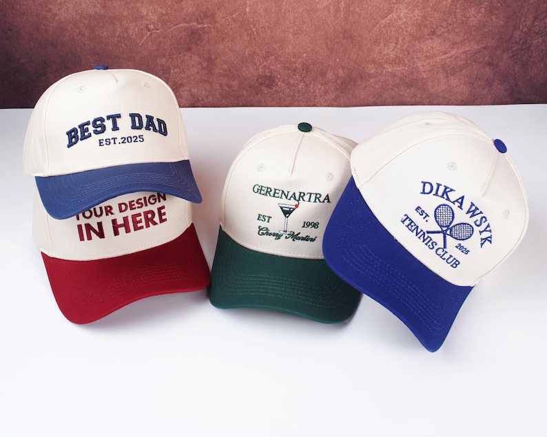 May include: Three baseball caps with embroidered designs. One cap is white with a blue brim and the text "BEST DAD EST.2025". Another is white with a green brim and a martini glass graphic. The third is white with a blue brim and "DIKAWSYK TENNIS CLUB".
