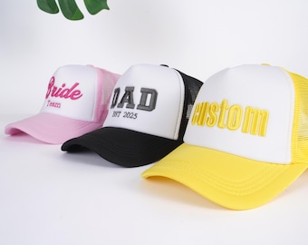 May include: Three trucker hats with white fronts and mesh backs. One pink hat has "Bride Team" embroidered in pink. A black and white hat has "DAD EST 2025" embroidered in gray. A yellow and white hat has "custom" embroidered in yellow.