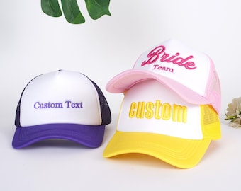 Puede incluir: Tres gorras de camionero con malla en la parte posterior. Una gorra es rosa con texto blanco que dice "Bride Team". Otra gorra es amarilla con texto blanco que dice "custom". La tercera gorra es morada con texto blanco que dice "Custom Text".