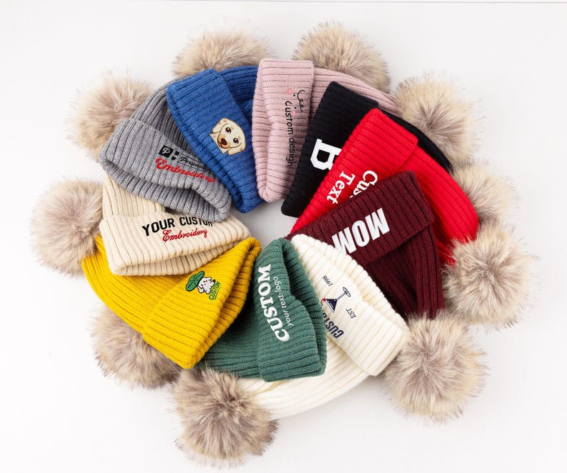 May include: A collection of ten ribbed knit beanies arranged in a circular pattern, each featuring a large faux fur pom-pom on top. The beanies come in various colors including gray, blue, pink, black, red, maroon, yellow, green, and white.