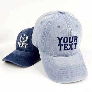 May include: Two denim baseball caps. One is a light blue wash with the text "YOUR TEXT" embroidered in navy blue. The other is a darker blue with the text "TEXT" and a "G" emblem embroidered in white.