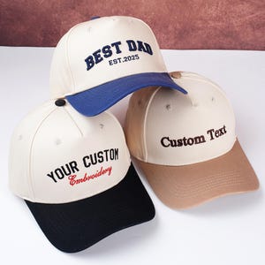 May include: Three baseball caps with embroidered text. One cap has "BEST DAD EST.2025" in navy blue, another says "YOUR CUSTOM Embroidery" in black and red, and the third says "Custom Text" in brown.