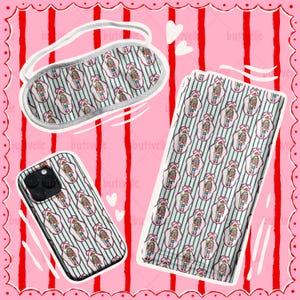 May include: A sleep mask, phone case, and a rectangular item with a repeating pattern of nutcracker figures on a striped background. The items are on a pink background with red stripes and white hearts.