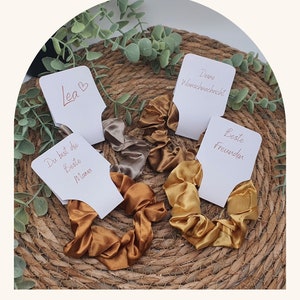 Könnte beinhalten: Vier Satin-Haargummis mit personalisierten Geschenkanhängern. Die Anhänger haben den Text "Du bist die Beste Mama", "Deine Wunschnachricht", "Beste Freundin" und "Lea".