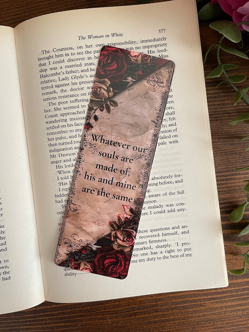 May include: A rectangular bookmark with a floral design featuring red and cream roses. The bookmark has a vintage aesthetic with script-style text that reads "Whatever our souls are made of, his and mine are the same."