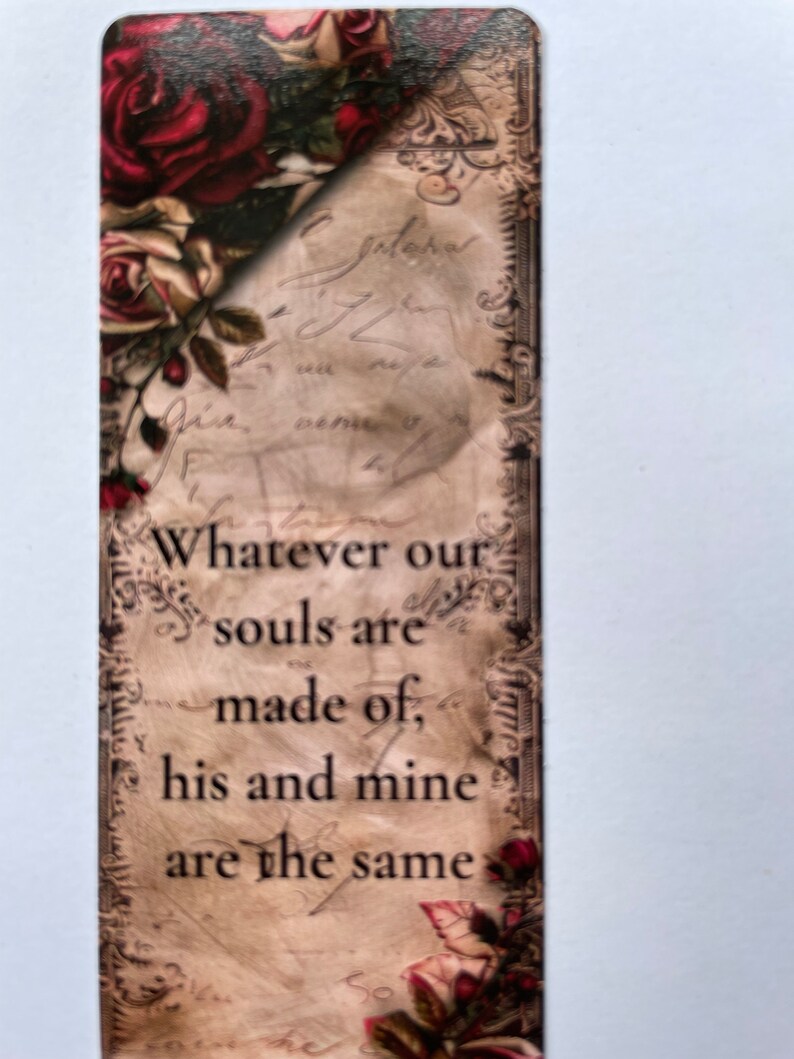 May include: A rectangular bookmark featuring a vintage-style parchment background with faded cursive script. The top left and bottom right corners are decorated with deep red and cream-colored roses. The text reads: Whatever our souls are made of, his and mine are the same.