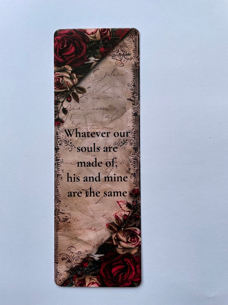 May include: A rectangular bookmark featuring a vintage-style background with cursive script and dark red roses at the top and bottom corners. The text reads: Whatever our souls are made of, his and mine are the same, printed in black.