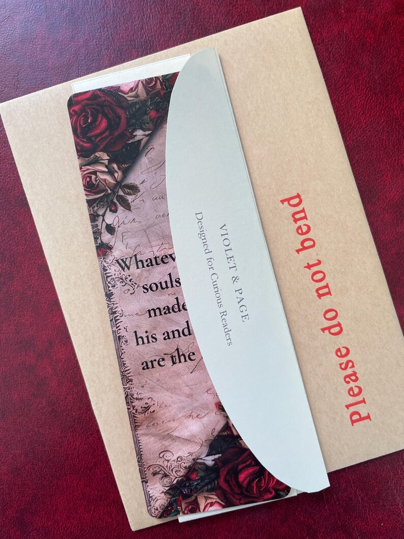May include: A bookmark featuring a floral rose pattern and vintage script text, partially covered by a curved white card with the text VIOLET & PAGE Designed for Curious Readers, all resting on a tan envelope labeled Please do not bend.