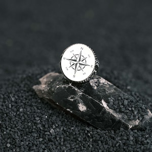 May include: A silver compass ring with a detailed compass design and the directions N, NE, E, SE, S, SW, W, NW engraved around the compass.