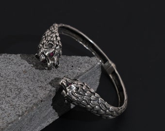 May include: Silver bracelet with two wolf heads on each end, each with red gemstone eyes.