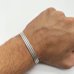 以下が含まれることがあります： シンプルでエレガントなデザインのシルバーブレスレット。ブレスレットは3つのシルバーバンドで構成されており、それぞれにわずかに異なるテクスチャがあります。