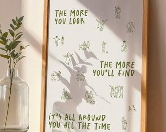 Puede incluir: Una impresión artística enmarcada con un fondo beige claro y texto e ilustraciones verdes. El texto dice: "CUANTO MÁS BUSCAS, MÁS ENCUENTRAS, ESTÁ A TU ALREDEDOR TODO EL TIEMPO". La impresión está en un marco de madera clara.