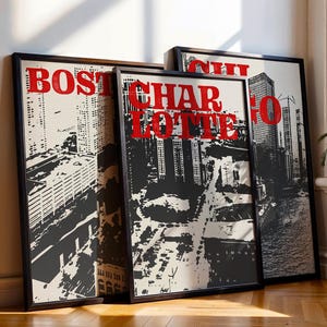 Könnte beinhalten: Drei gerahmte Stadtposter mit schwarzen Rahmen lehnen an einer weißen Wand. Die Poster zeigen eine schwarz-weiße Stadtlandschaft mit rotem Text, der "BOSTON", "CHARLOTTE" und "CHI" lautet. Die Poster werden in der Nähe eines Fensters mit einer Topfpflanze ausgestellt.