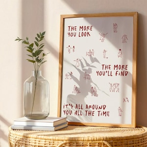 Puede incluir: Una impresi&oacute;n art&iacute;stica enmarcada con el texto rojo "THE MORE YOU LOOK, THE MORE YOU'LL FIND, IT'S ALL AROUND YOU ALL THE TIME". La impresi&oacute;n presenta peque&ntilde;as ilustraciones rojas de personas. A la izquierda hay un jarr&oacute;n de cristal transparente con vegetaci&oacute;n.