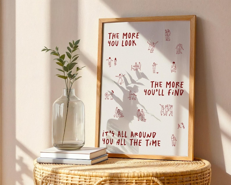 Puede incluir: Una impresi&oacute;n art&iacute;stica enmarcada con el texto rojo "THE MORE YOU LOOK, THE MORE YOU'LL FIND, IT'S ALL AROUND YOU ALL THE TIME". La impresi&oacute;n presenta peque&ntilde;as ilustraciones rojas de personas. A la izquierda hay un jarr&oacute;n de cristal transparente con vegetaci&oacute;n.