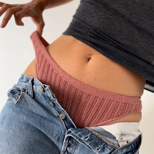 Puede incluir: Un par de ropa interior de punto de canalé en color rosa polvoriento. La ropa interior se saca parcialmente de un par de pantalones vaqueros azules.