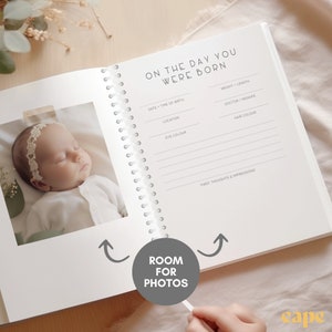 May include: Open baby memory book with a photo of a sleeping infant. The book has a spiral binding and prompts to record details like date, time of birth, and eye color. The text "ON THE DAY YOU WERE BORN" is at the top.