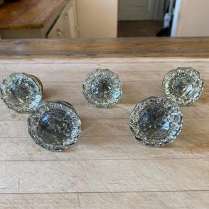 May include: Five clear glass door knobs with a faceted design. The knobs have a brass base.