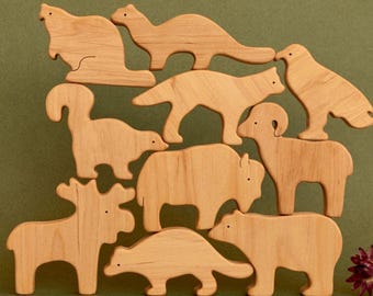 Könnte beinhalten: Eine Sammlung von Holzfiguren von Tieren, darunter ein Biber, ein Eichhörnchen, ein Wolf, ein Widder, ein Bison, ein Bär, ein Elch, ein Dachs und ein Vogel. Die Figuren sind aus hellem Holz gefertigt und auf grünem Grund angeordnet.