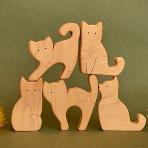 May include: Five wooden cat figurines stacked on top of each other. The cats are all different sizes and shapes, and they are all made of natural wood.