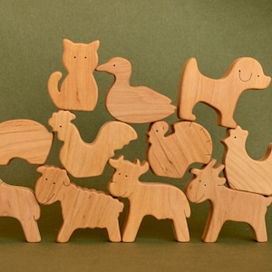 Op de afbeelding: Houten boerderijdieren speelgoed, waaronder een kat, eend, hond, varken, haan, kalkoen, kip, paard, schaap en koeien. Het speelgoed is gemaakt van lichtgekleurd hout en geplaatst op een groene achtergrond.
