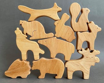May include: A set of ten wooden animal puzzle pieces, including a fox, rabbit, squirrel, deer, bear, moose, wolf, raccoon, hedgehog, and a bear. The pieces are all natural wood color and are stacked on top of each other.