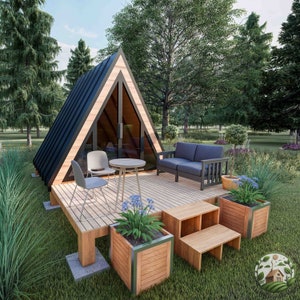 May include: A small, triangular wooden cabin with a black roof and large windows. The cabin has a wooden deck with a table and chairs, a couch, and potted plants.