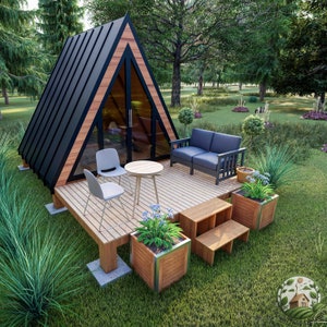 May include: A small, black and wood A-frame cabin with a wooden deck and a black metal sofa. The cabin has large windows and a black roof. There are two white chairs and a small table on the deck. There are two potted plants on the deck, one with blue flowers.