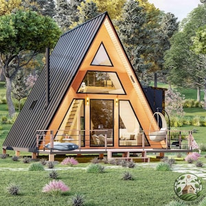 May include: A small, wooden A-frame cabin with a black roof and large windows. The cabin is surrounded by green grass and trees. There is a small deck in front of the cabin with a hanging chair.