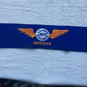 May include: Blue patch with a white circle containing the text "U.S. ARMY AWS AIR FORCE" and an orange winged design. The text "OBSERVER" is below the circle.