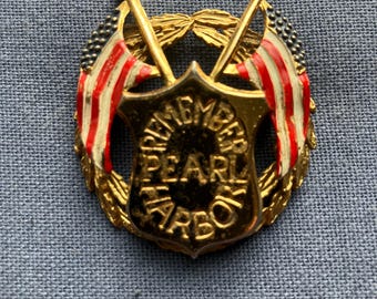 May include: A gold-toned pin with a shield design, featuring the text "REMEMBER PEARL HARBOR." Two American flags with red and white stripes and blue stars flank the shield. The pin is surrounded by a gold wreath.