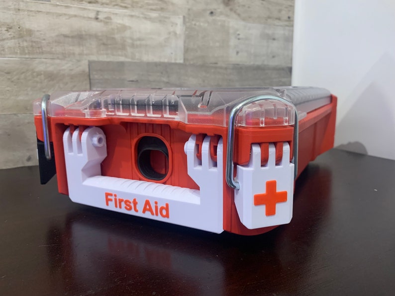 May include: A red and white plastic first aid kit with a clear lid and a white handle. The kit has a red cross on the side and the words "First Aid" printed on the front.