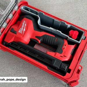 Peut inclure: Un cloueur sans fil Milwaukee rouge et noir dans un coffret rigide rouge avec un insert en mousse grise. Le coffret est ouvert et le cloueur est à l'intérieur.