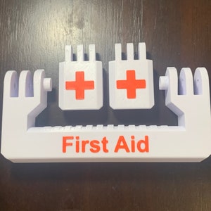 May include: White plastic first aid kit holder with two red crosses and the words "First Aid" printed in red.