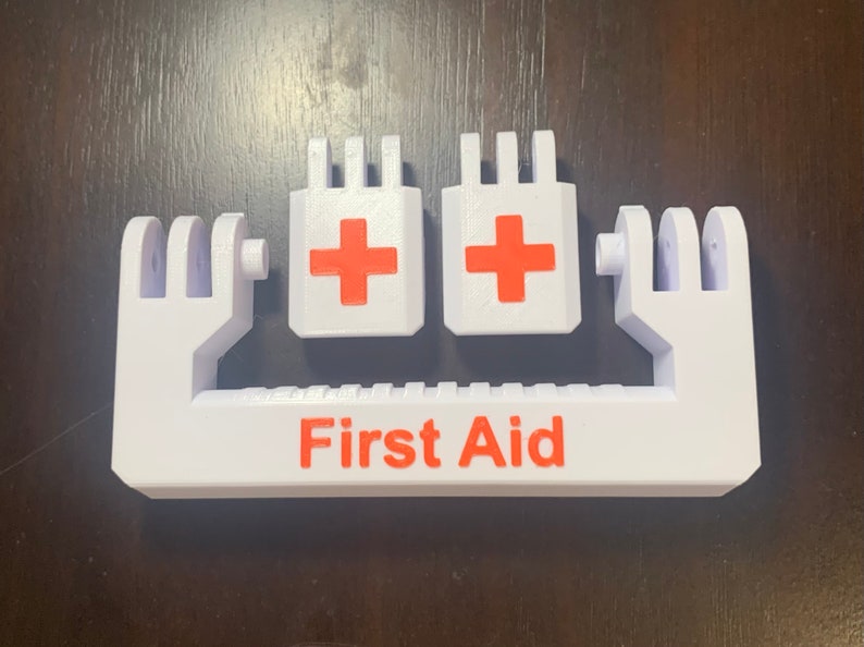 May include: White plastic first aid kit holder with two red crosses and the words "First Aid" printed in red.