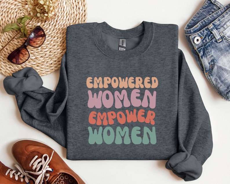 May include: A dark gray sweatshirt with the text "EMPOWERED WOMEN EMPOWER WOMEN" in a retro, colorful font.