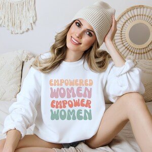 May include: White sweatshirt with the text "EMPOWERED WOMEN EMPOWER WOMEN" in a retro font with pink, orange, and green colors.