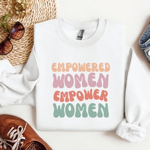 May include: White sweatshirt with the text "Empowered Women Empower Women" in colorful, retro-style lettering.