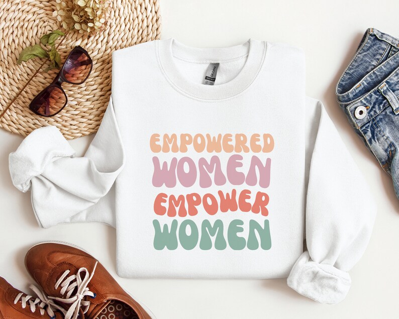 May include: White sweatshirt with the text "Empowered Women Empower Women" in colorful, retro-style lettering.