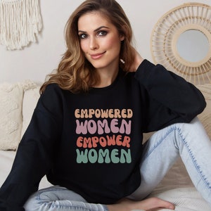 May include: A black sweatshirt with the text "EMPOWERED WOMEN EMPOWER WOMEN" in a retro font with pink, orange, and green colors.