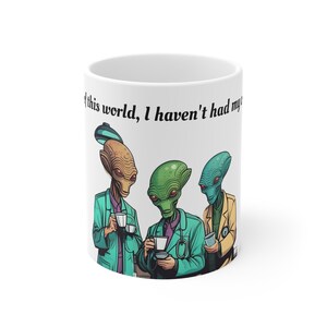 May include: White ceramic mug with a graphic of three aliens drinking coffee. The text on the mug reads "of this world, I haven't had my coffee".
