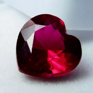 Puede incluir: Una gema facetada en forma de corazón, de un tono rojo intenso. La gema tiene múltiples superficies reflectantes, creando un efecto brillante. La forma es simétrica, con una parte superior redondeada y una base puntiaguda.