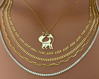 May include: A gold chain necklace with a fox pendant. The pendant has the name "Megan" engraved on it. The necklace is layered with other gold chains and a diamond chain.
