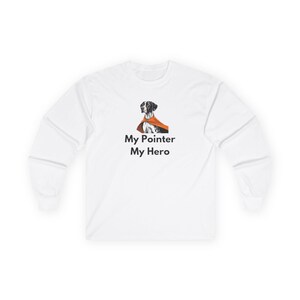 Könnte beinhalten: Weißes Langarmshirt mit einer Grafik eines Pointer-Hundes, der einen orangefarbenen Umhang trägt. Der Text "My Pointer My Hero" ist unter der Hundeillustration aufgedruckt. Das Shirt hat einen Rundhalsausschnitt und lange Ärmel.