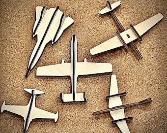 May include: Five wooden airplane models in various styles. The models are painted black and white and are arranged on a brown surface.
