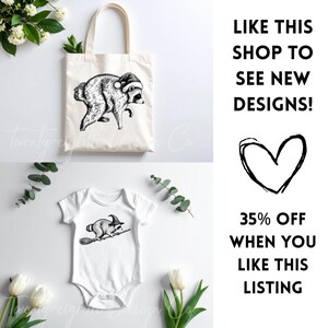 May include: A white canvas tote bag featuring a black and white illustration of a raccoon wearing a Santa hat, and a white baby bodysuit featuring a black and white illustration of a raccoon wearing a witch hat and riding a broomstick.