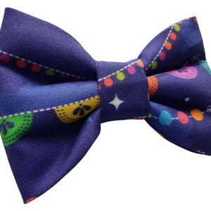 May include: A purple bow tie with a colorful string of lights pattern. The lights are yellow, orange, pink, blue, and green.
